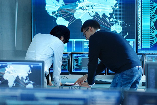 In the System Control Room Project Manage and IT Engineer Have Discussion, they're surrounded by Multiple Monitors with Graphics. Big Monitor Shows Interactive Logistics Map.