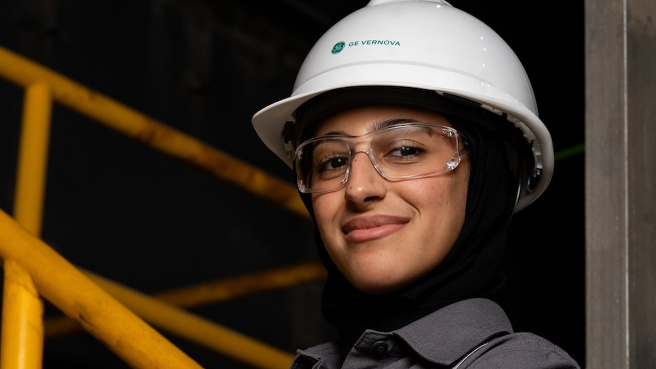 A woman with helment and safety glasses smiles to camera