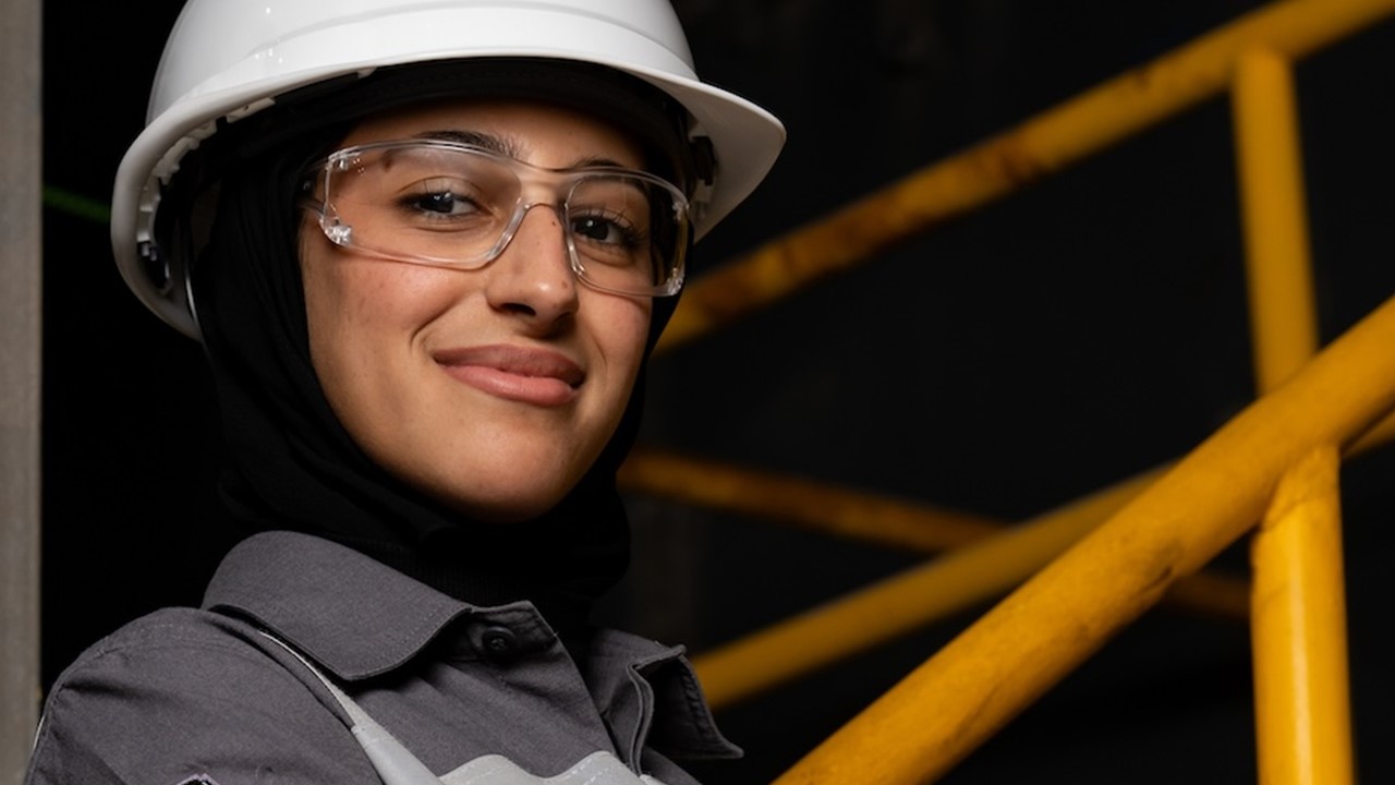 Woman with helmet and safety glasses smiles to camera with confidence