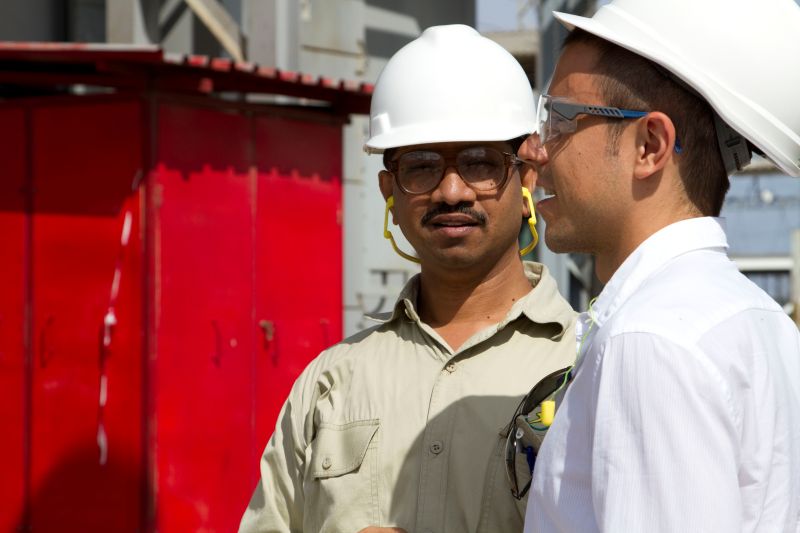 Two men in white hardhats talking outside close together