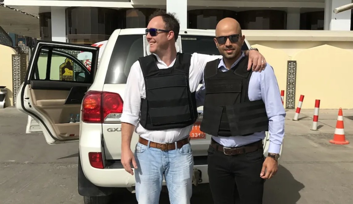 Two men in black vests with arms around each other