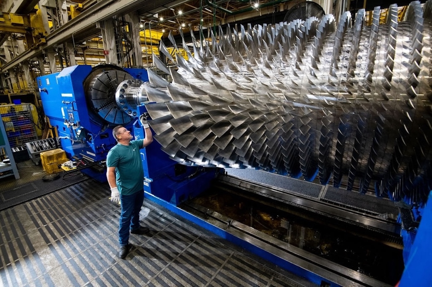 A technician inspecting a massive power-generating turbine rotor designed to reduce global grid carbon intensity.