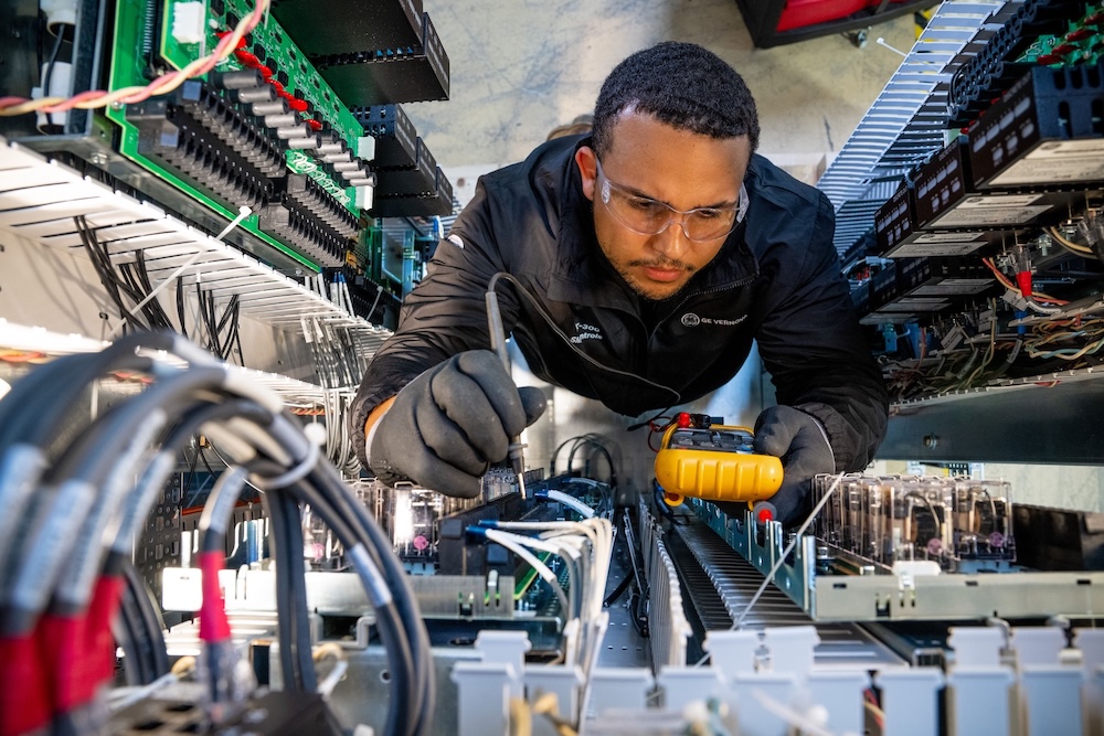 An electrical technician using a multimeter to test complex wiring for low-emissions infrastructure and grid modernization