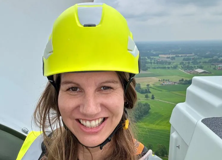 Woman in a yellow hard hat taking a selfie on top of a windmill