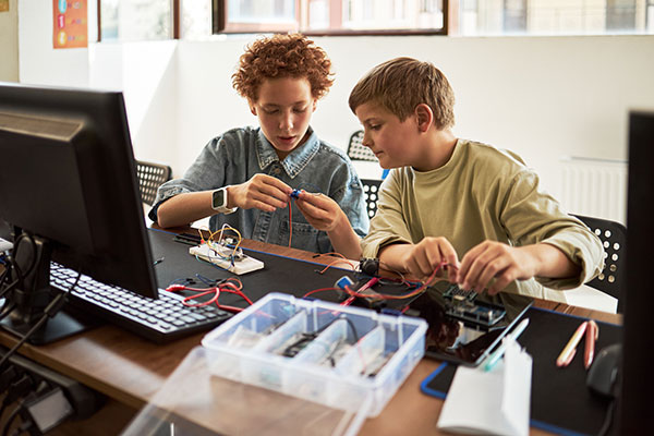 Two boys working together assembling electronic components at desk in classroom